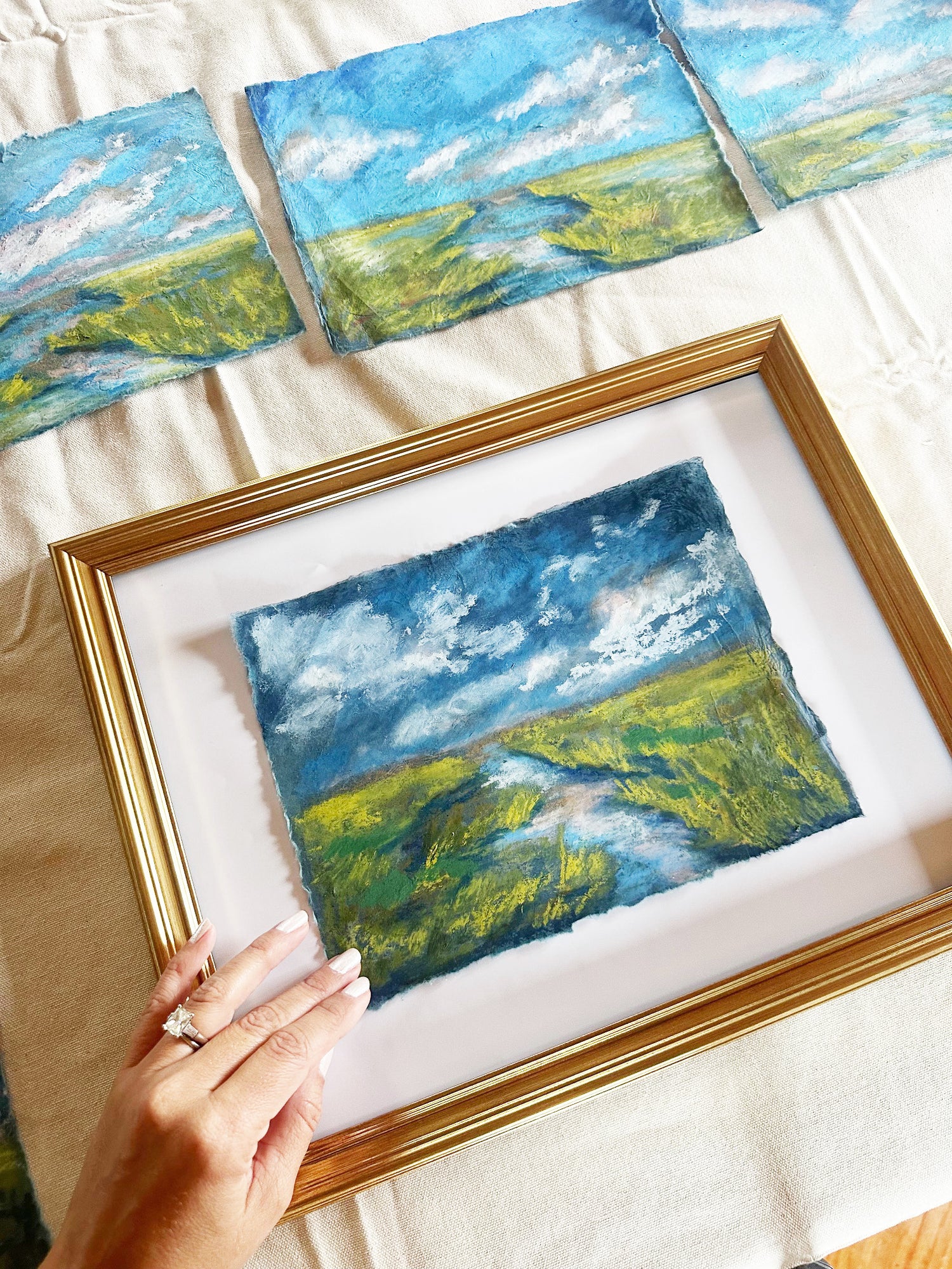 Framed landscape painting with a hand adjusting it on a light background