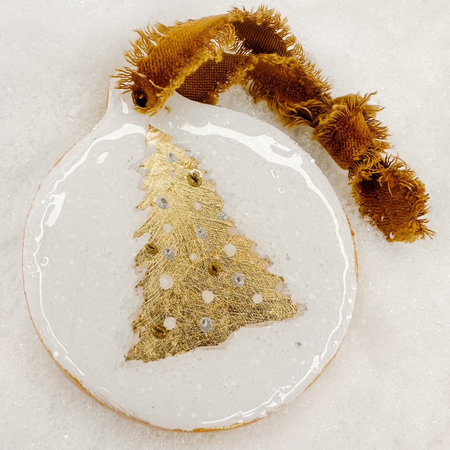Decorative ornament with gold tree design and brown ribbon on a light background