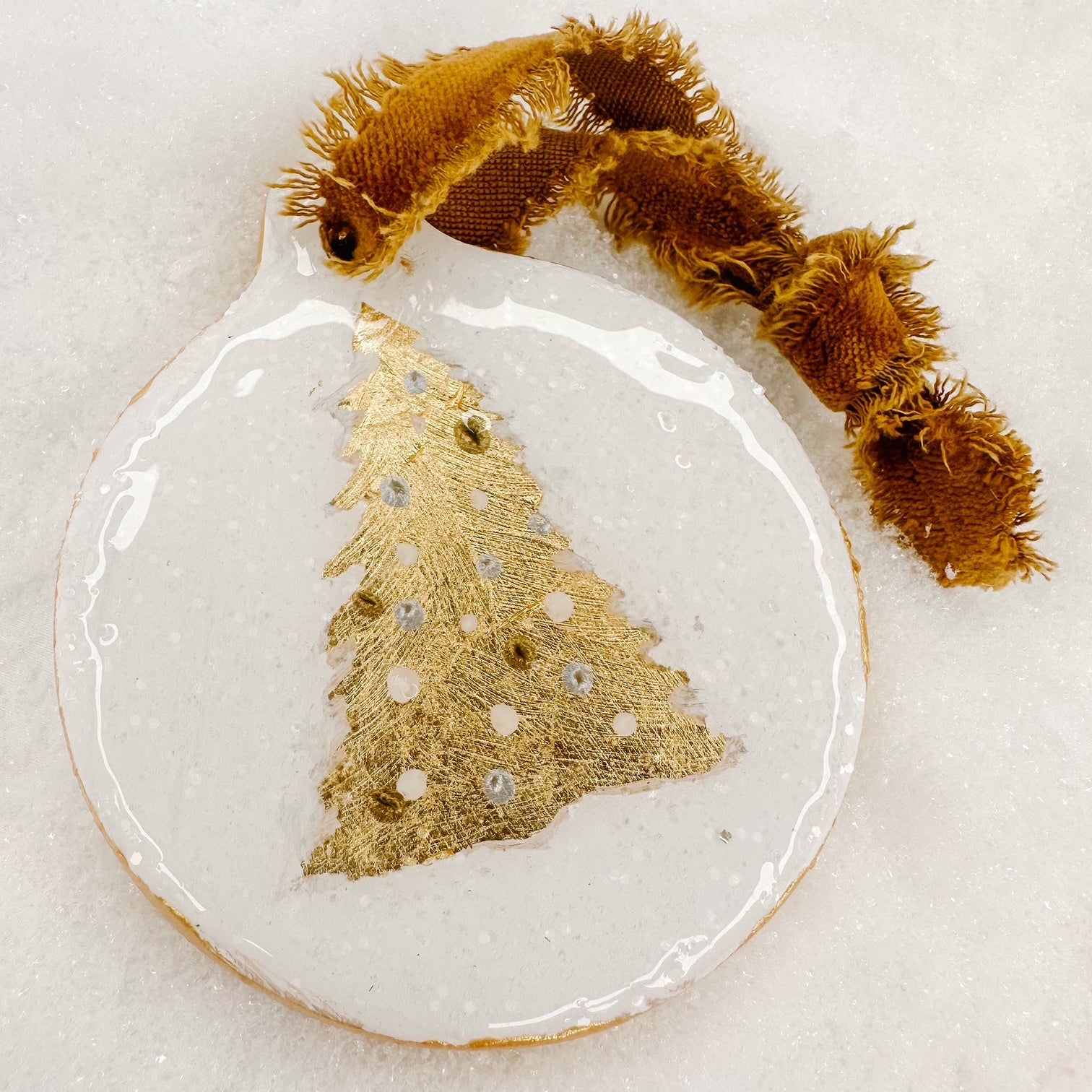 Decorative ornament with gold tree design and brown ribbon on a light background