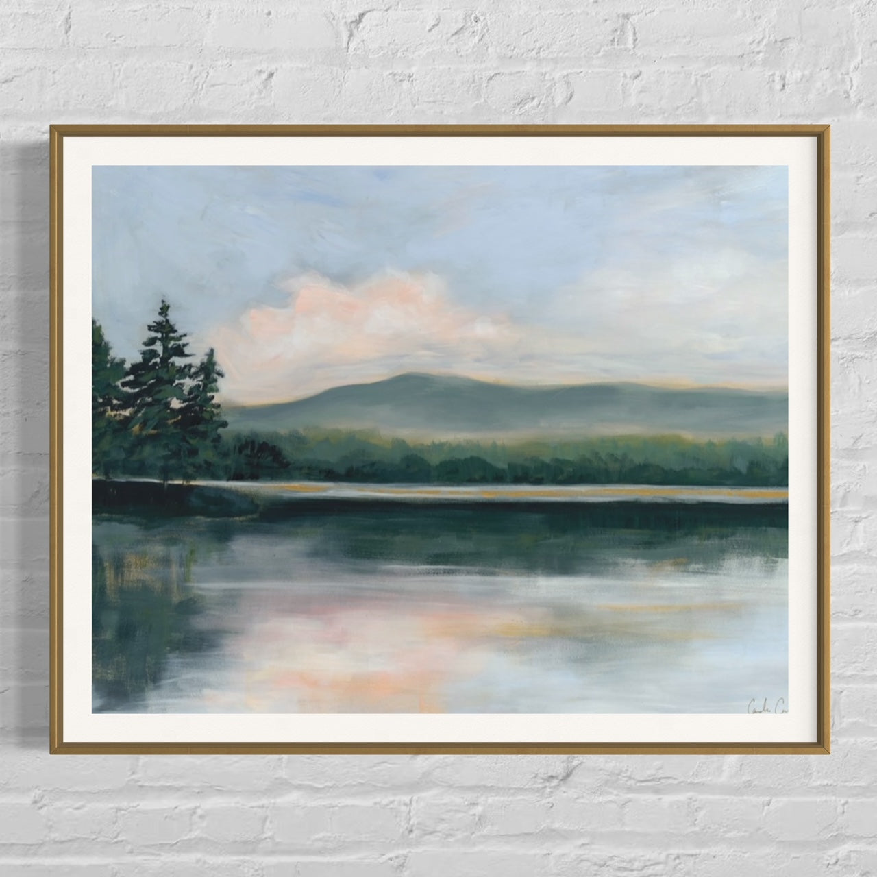 Fine art print of serene lake surrounded by evergreen trees during the golden hour of sunset framed in gold on painted brick wall