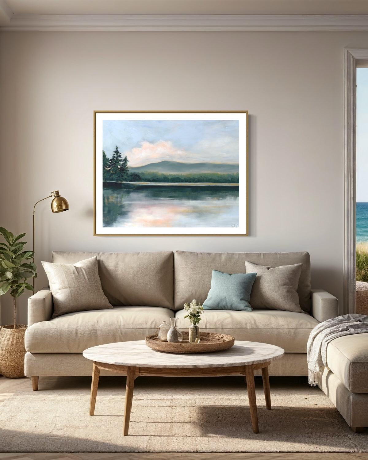 Fine art print of serene lake surrounded by evergreen trees during the golden hour of sunset hung above tan sofa